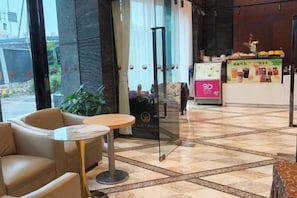 A hotel lobby with a reception desk, a seating area with a round table, and a glass door entrance. - Grand Daqiao Hotel (Nanjing)