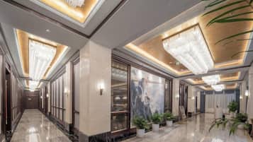 A hotel lobby with a marble floor, large chandeliers, and potted plants.