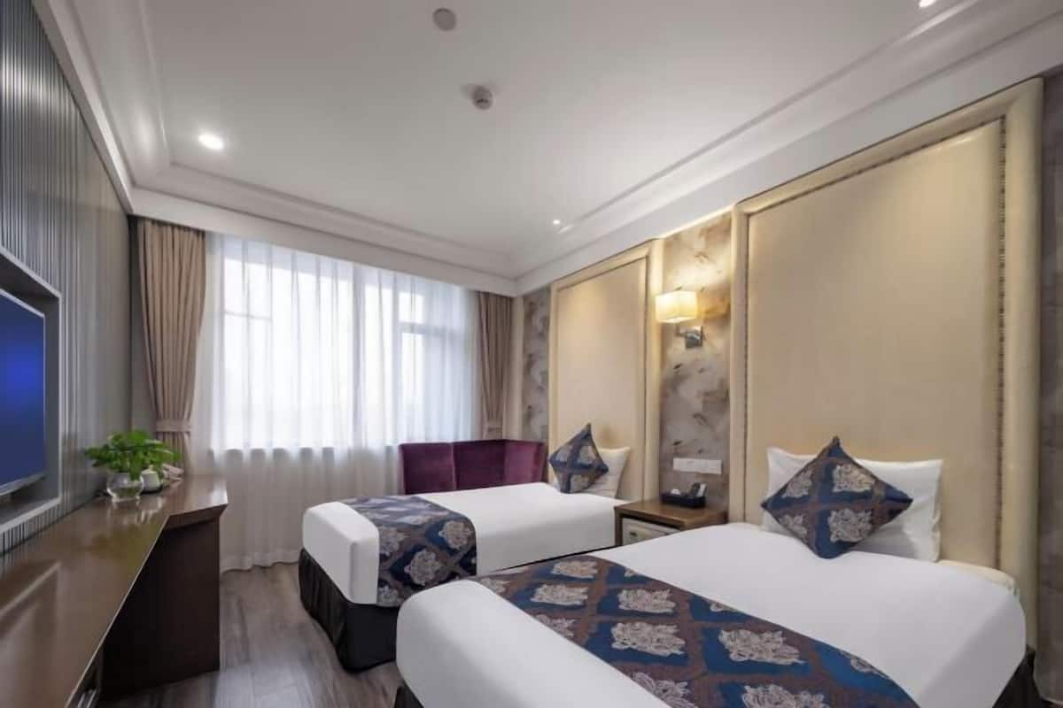 Habitación de hotel con dos camas, un escritorio, un televisor y una ventana con cortinas.