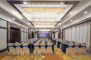A conference room with rows of tables and chairs, a large chandelier, and a presentation screen at the front. - Grand Daqiao Hotel (Nanjing)