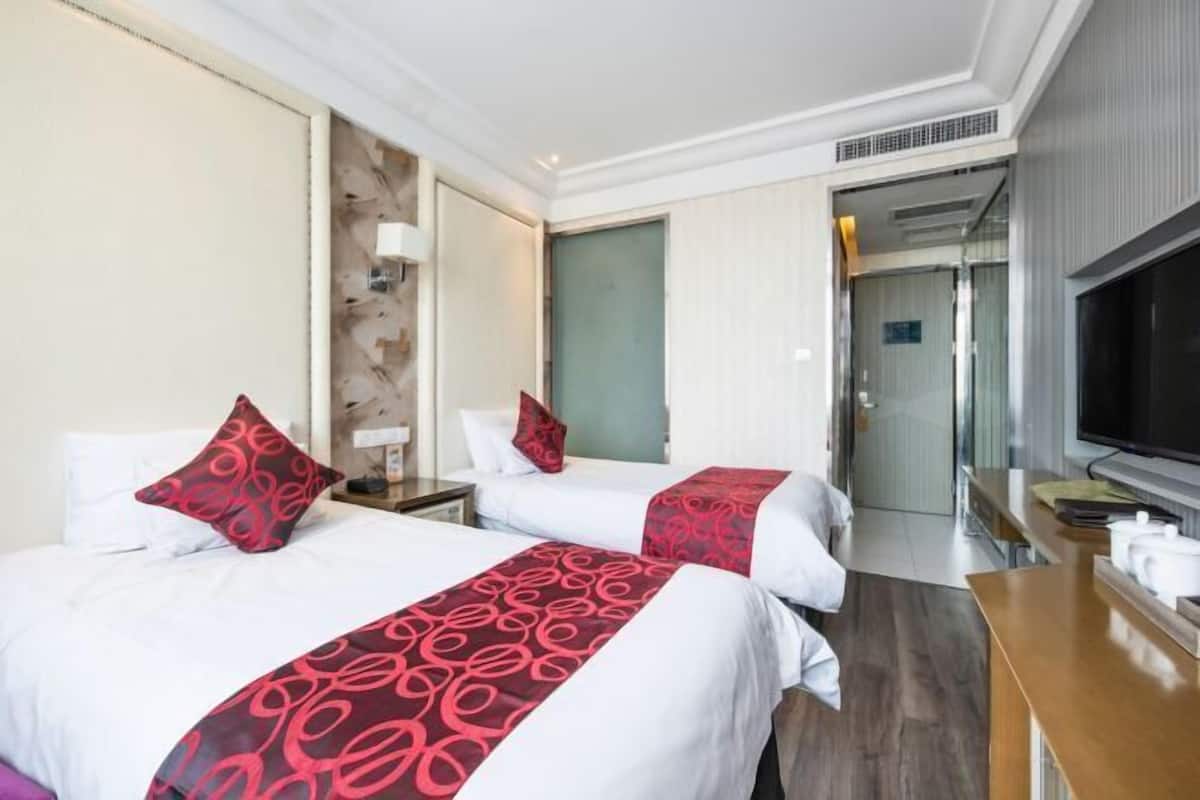 Habitación de hotel con dos camas, televisor, escritorio y baño visible a través de una puerta abierta.