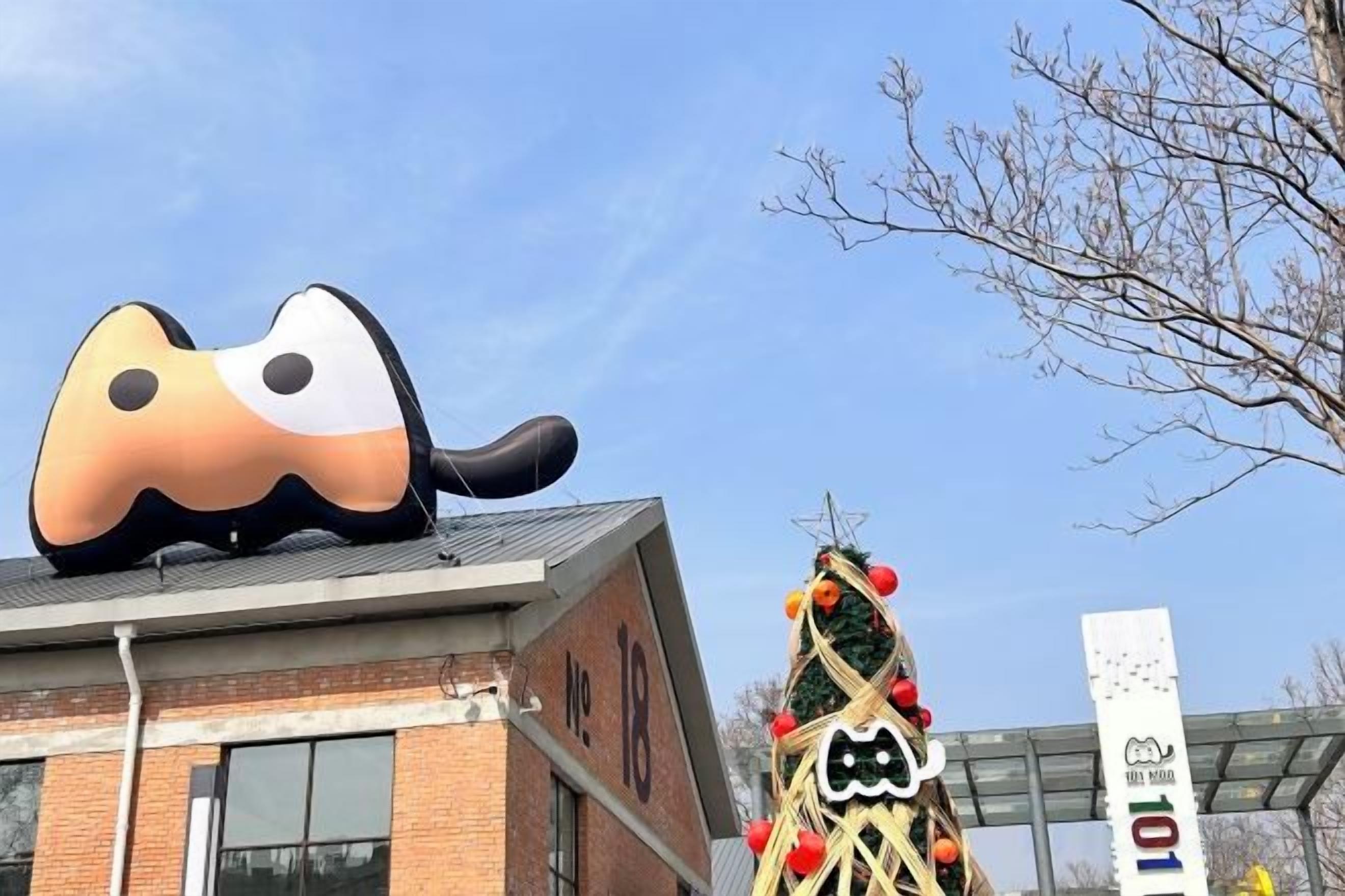 A building with a large inflatable animal decoration on the roof, a Christmas tree with lights, and a sign with a logo and number.