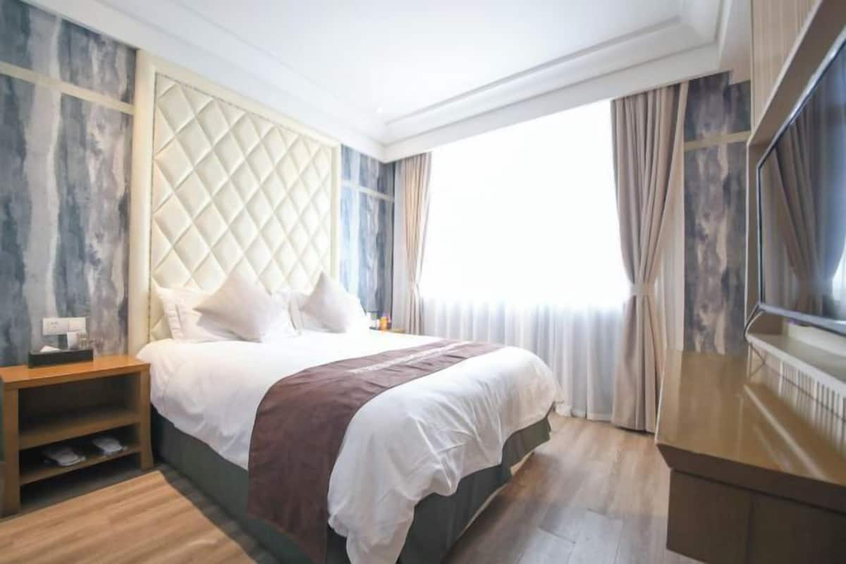 Habitación de hotel con cama, mesita de noche, televisor y ventana con cortinas.