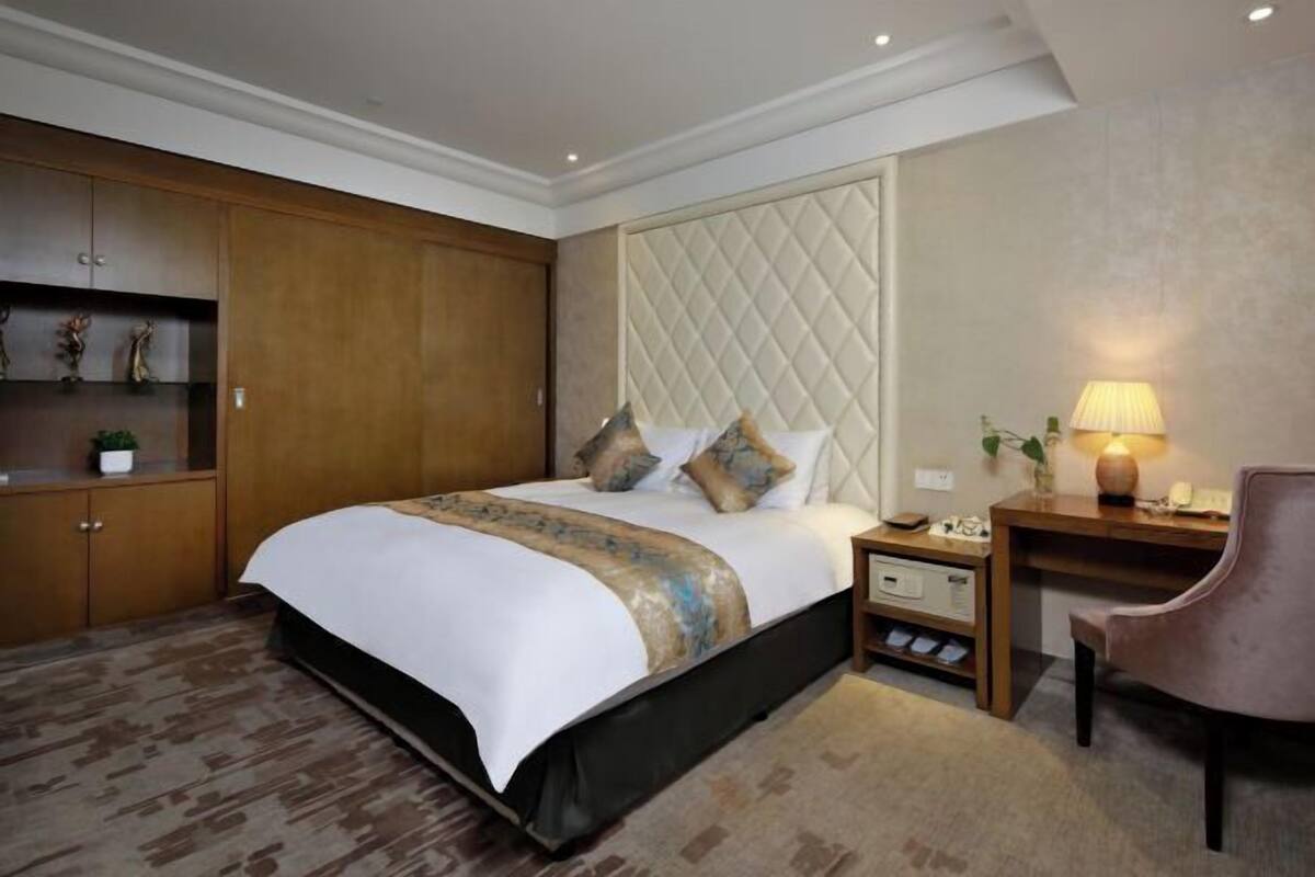 Habitación de hotel con cama, mesita de noche, lámpara, silla y armario empotrado.