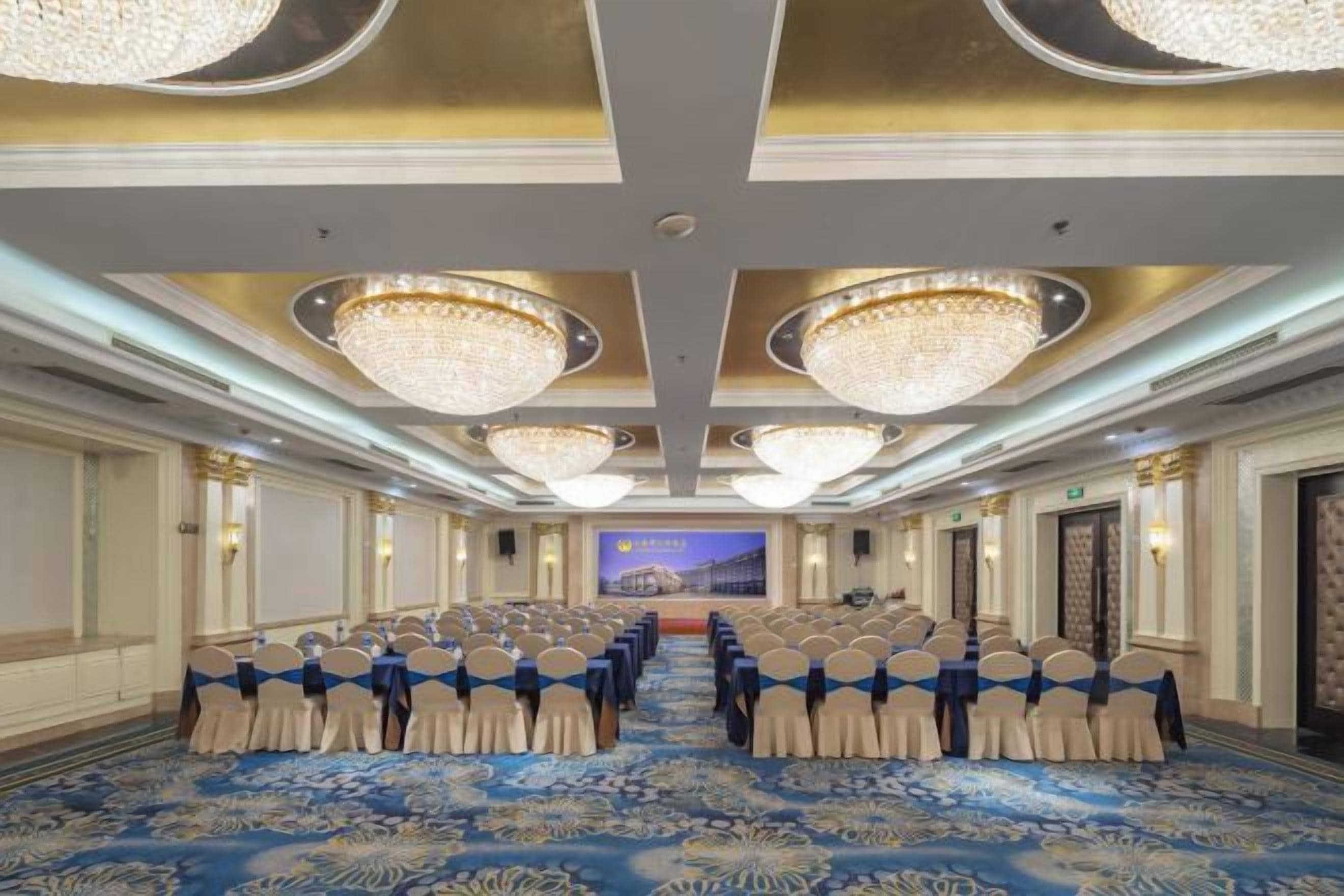 Un salón de conferencias con filas de sillas, un escenario y candelabros.