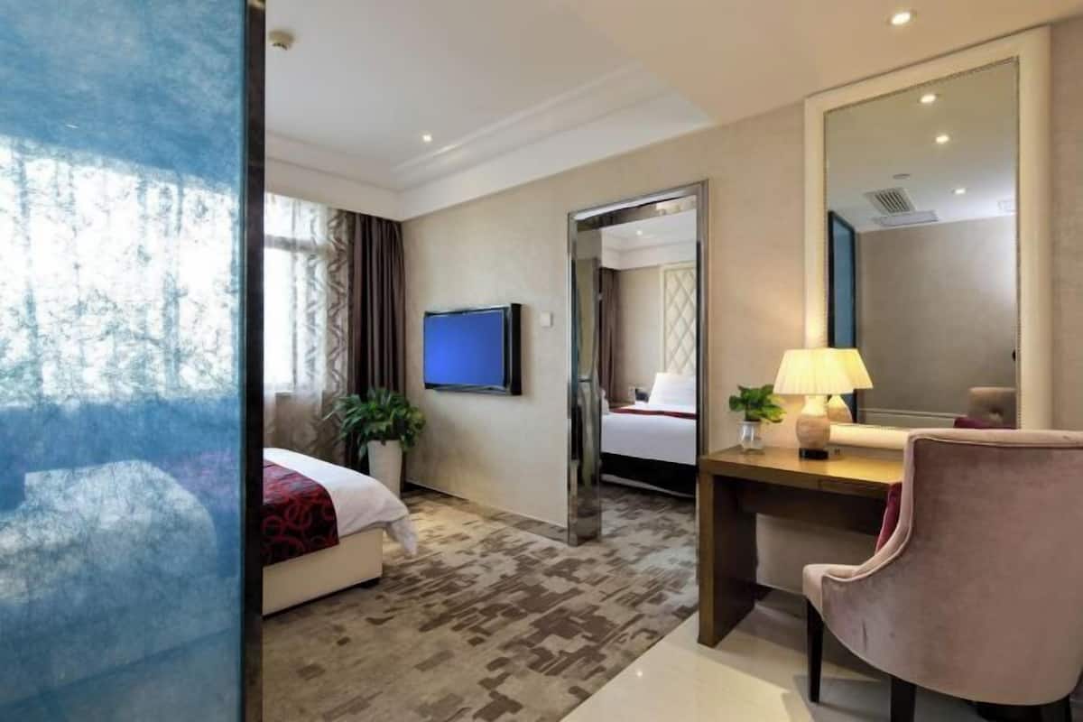 Una habitación de hotel con cama, escritorio, silla, televisor y un espejo grande.