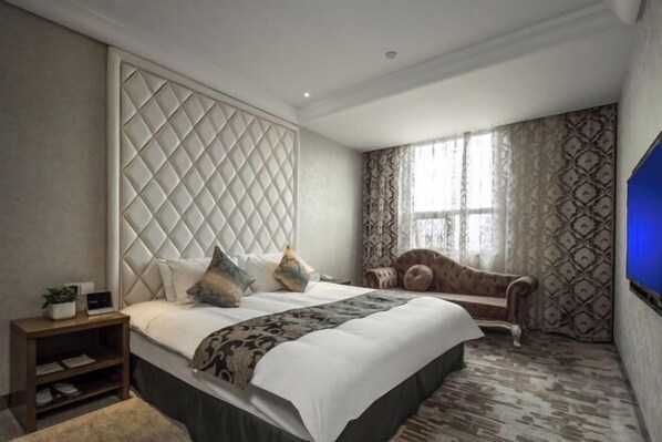A hotel room with a large bed, a nightstand, a sofa, and a TV.