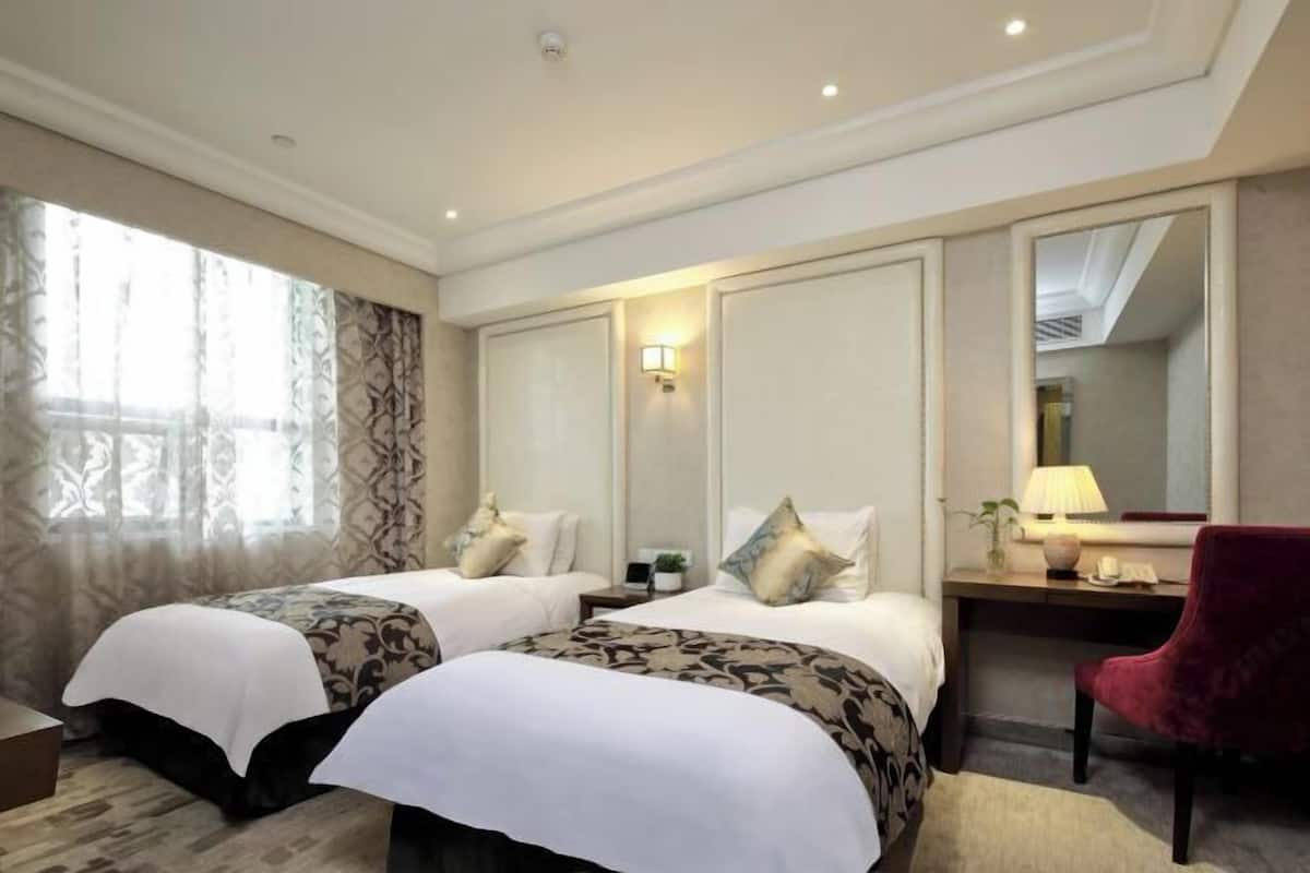 Habitación de hotel con dos camas, un escritorio, una silla, un espejo y una ventana con cortinas.