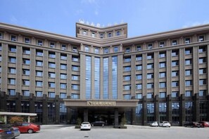 Un edificio grande de varios pisos con fachada simétrica, entrada central y estacionamiento al frente.