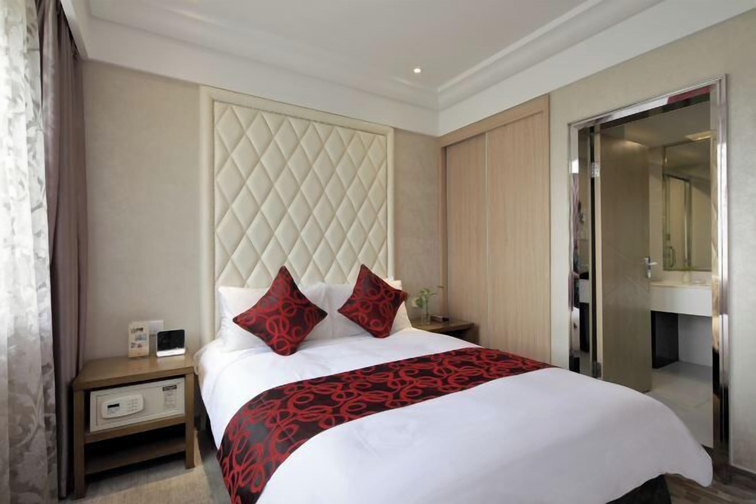 A hotel room with a large bed, a nightstand, a wardrobe, and a bathroom visible through an open door.