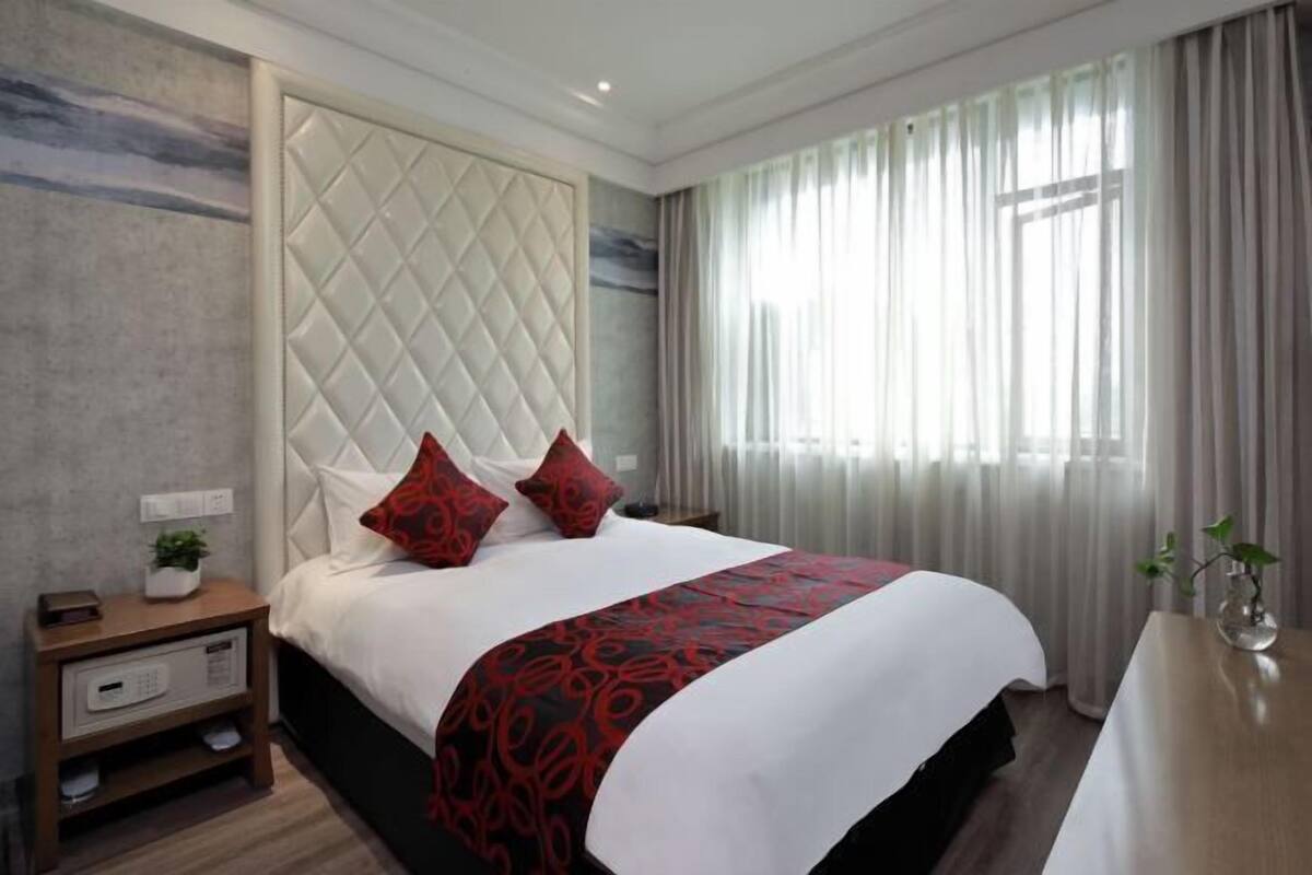 Una habitación de hotel con una cama grande, una mesita de noche y un ventanal con cortinas.