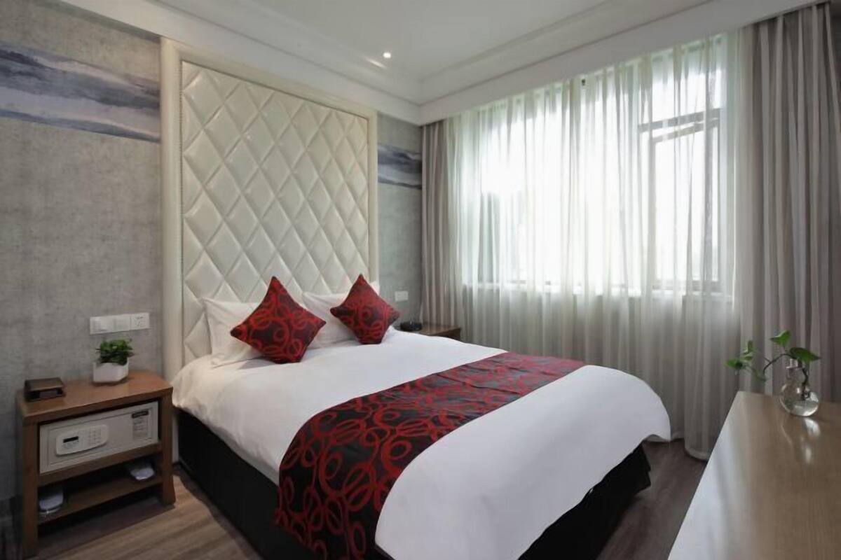 Una habitación de hotel moderna con una cama grande, una mesita de noche y un ventanal con cortinas.