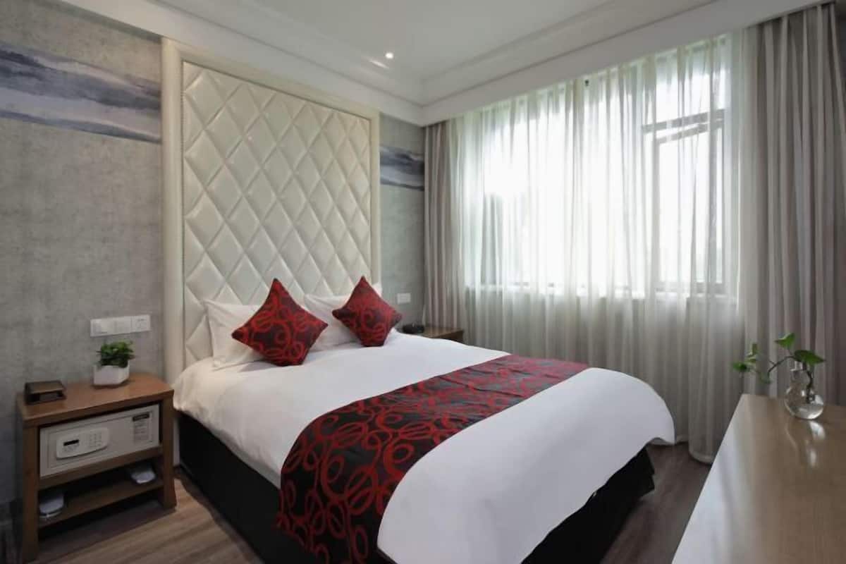 Une chambre d’hôtel moderne avec un grand lit, une table de chevet, une commode et une fenêtre avec des rideaux.