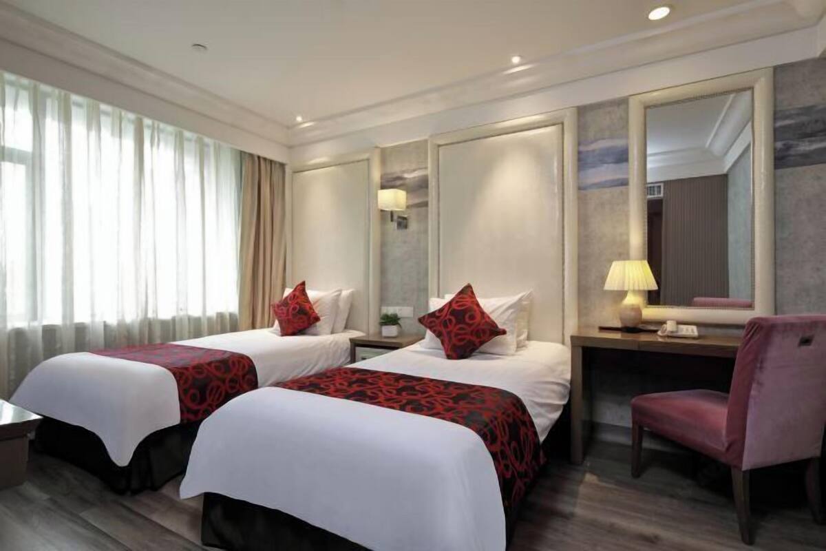Habitación de hotel con dos camas, un escritorio, una silla y un espejo grande.