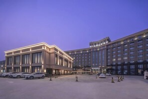 Een groot hotel met meerdere verdiepingen, een parkeerplaats en een heldere lucht.