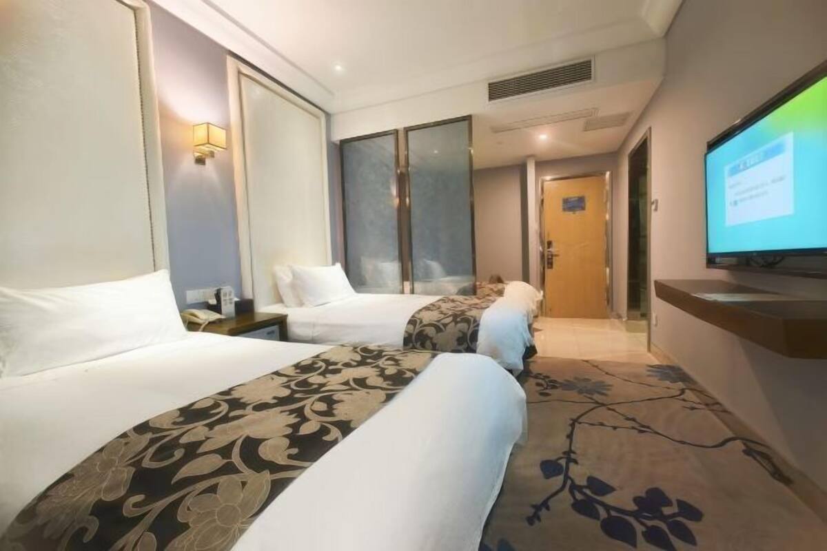 Habitación de hotel con dos camas, televisión, escritorio y un ventanal grande.