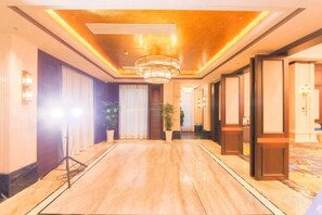 A hotel corridor with a chandelier, potted plants, and a carpeted floor. - Grand Daqiao Hotel (Nanjing)