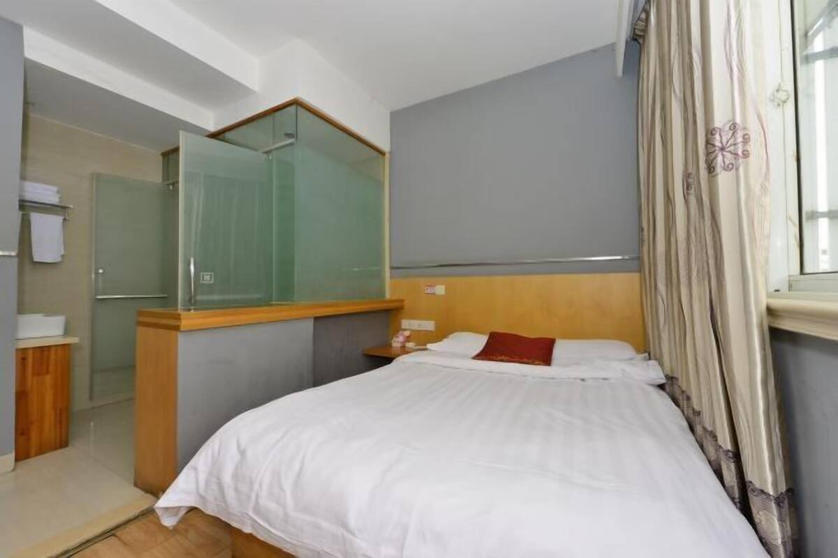 A hotel room with a bed, a nightstand, a mirror, a shower, and a window with curtains.