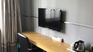 A room with a wooden desk, a black chair, a flat-screen TV mounted on the wall, a kettle, and a cup on a tray. - Xiangshan Shipu Hongting Hotel (Xiangshan)