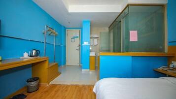 A hotel room with a bed, a desk, a chair, a trash bin, and a window.
