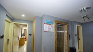 A hallway with a door leading to a room, a poster on the wall, and an elevator. - Xiangshan Shipu Hongting Hotel (Xiangshan)
