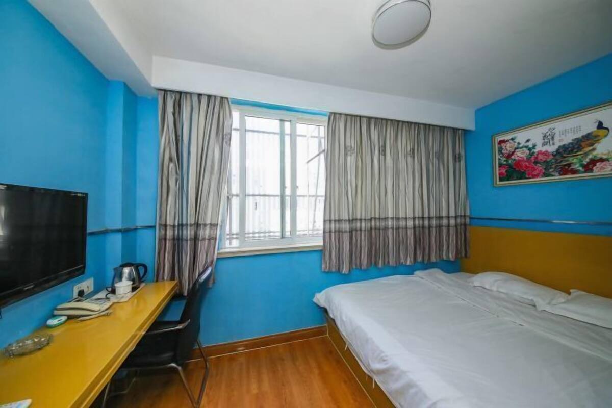 A room with a bed, a desk with a television, and a window with curtains.