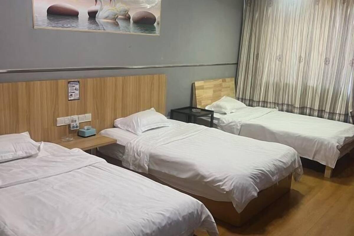 A hotel room with two single beds, a wooden headboard, a nightstand with a lamp, and a painting of a serene landscape.