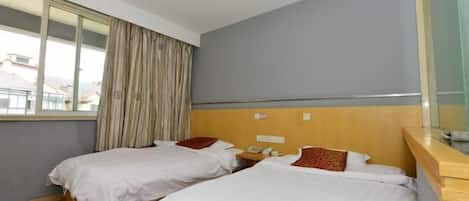 A hotel room with two single beds, a wooden headboard, a bedside table with a phone, and a window with curtains.