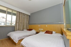 Habitación de hotel con dos camas individuales, cabecero de madera, mesita de noche con teléfono y ventana con cortinas.