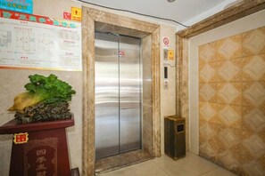 Egy digitális kijelzővel ellátott lift, egy falinaptár és egy dísznövény egy talapzaton.