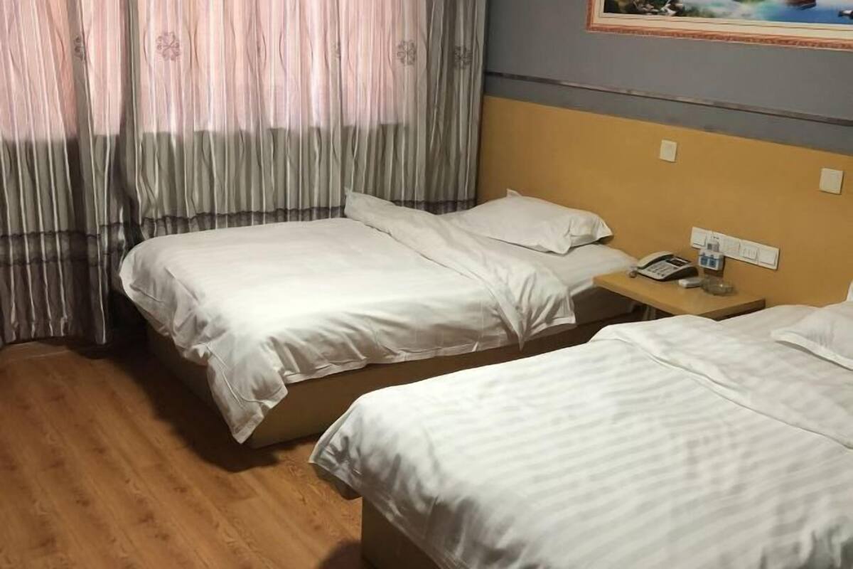 A hotel room with two beds, a wooden floor, a nightstand with a phone, and a painting on the wall.