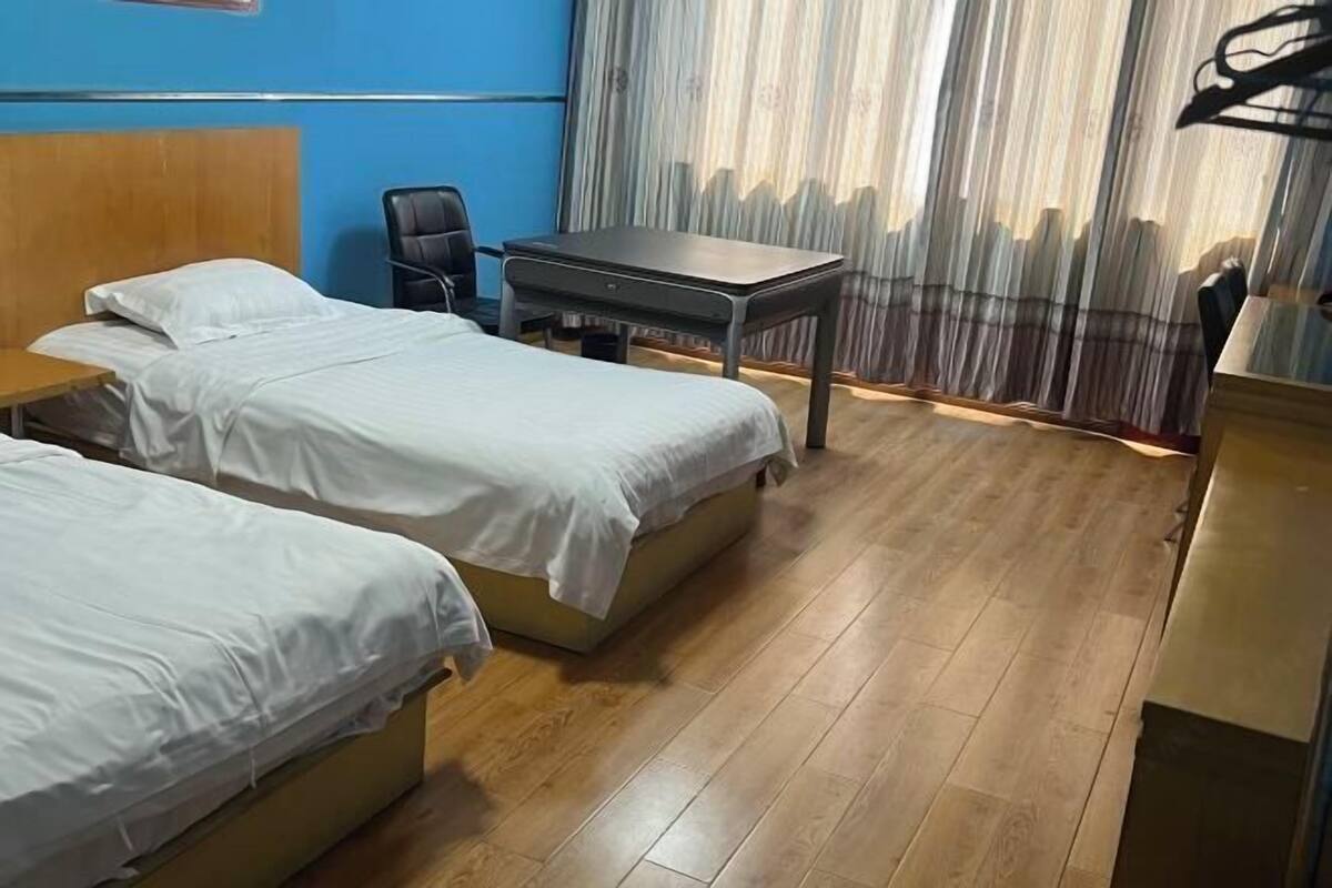 A hotel room with two beds, a desk, a chair, and a curtain.