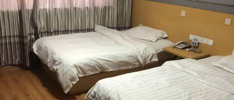 Habitación de hotel con dos camas individuales, piso de madera, mesita de noche con teléfono y un cuadro en la pared.