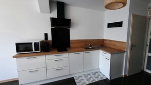 Une cuisine compacte avec des meubles blancs, un four à micro-ondes, une hotte noire et un plan de travail en bois.