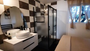 Une salle de bain avec un carrelage à motifs géométriques, un grand miroir, deux lavabos, un espace douche et une fenêtre avec des rideaux.