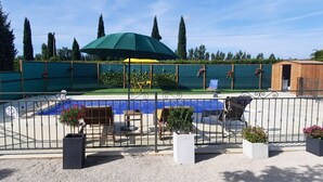 Un espace piscine agrémenté d’un parasol vert, de sièges et de plantes en pot.