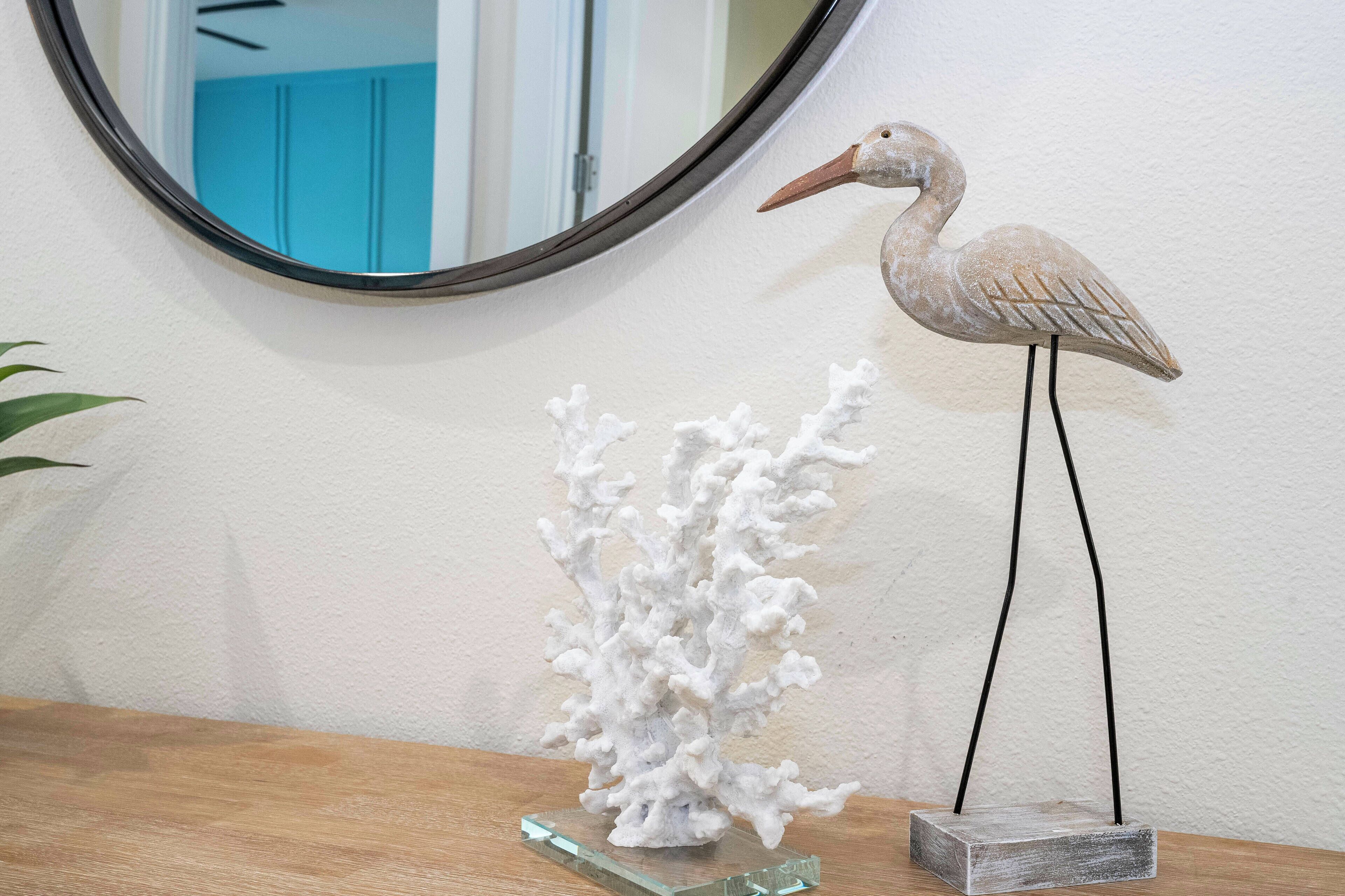 Une sculpture décorative représentant un oiseau, posée sur un socle, une structure blanche évoquant des coraux et un miroir fixé au mur.