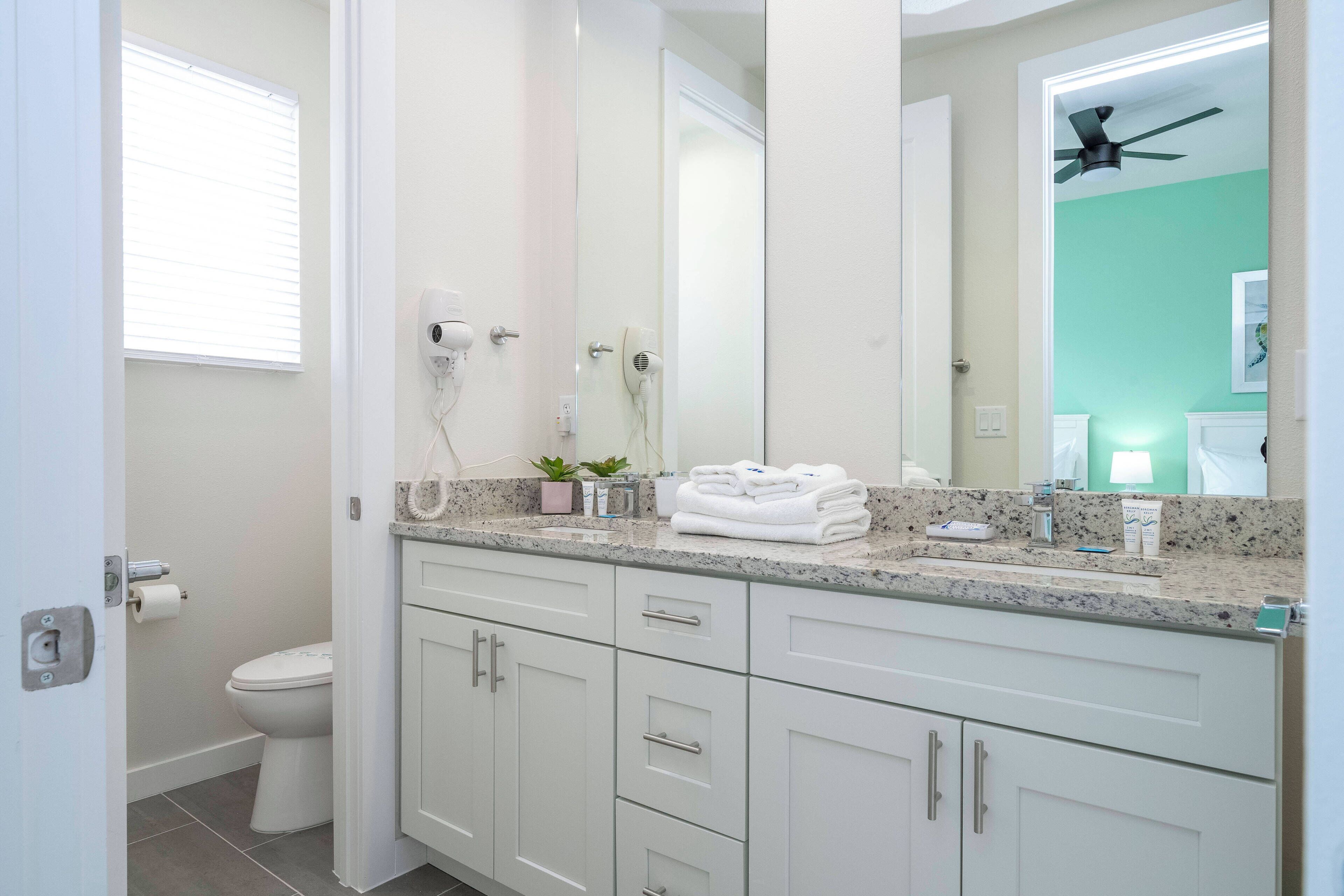 A bathroom with a white toilet, a sink with a granite countertop, and a mirror above the sink.
