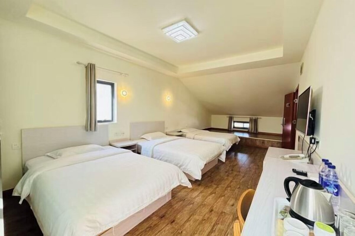 A hotel room with three beds, a desk with a kettle, and a TV.