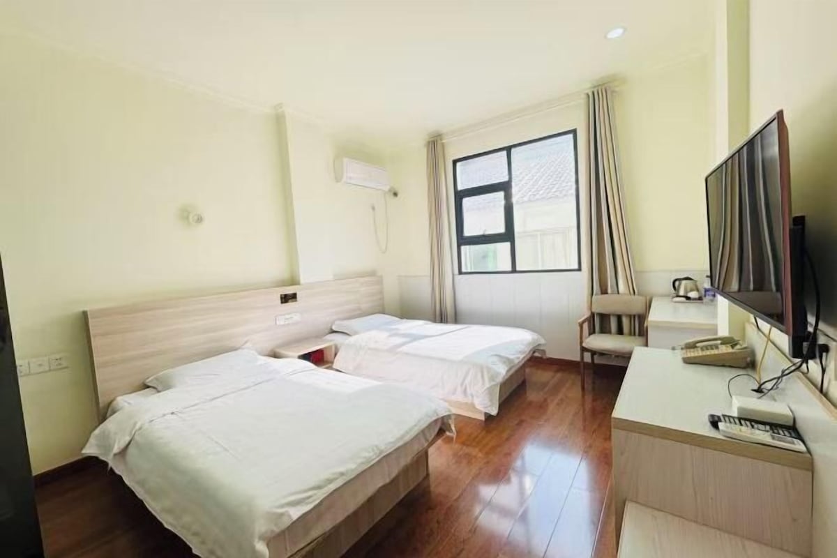 A hotel room with two beds, a desk with a computer, a TV, and a window with curtains.