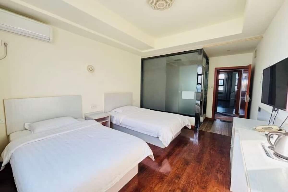 A hotel room with two beds, a TV, a desk, and a wooden floor.