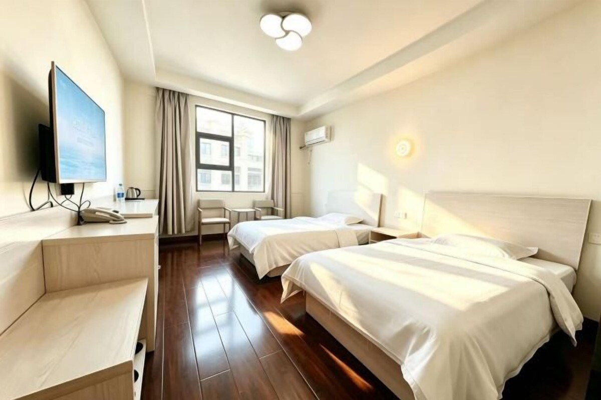 A hotel room with two beds, a desk, a chair, a TV, and a window with curtains.