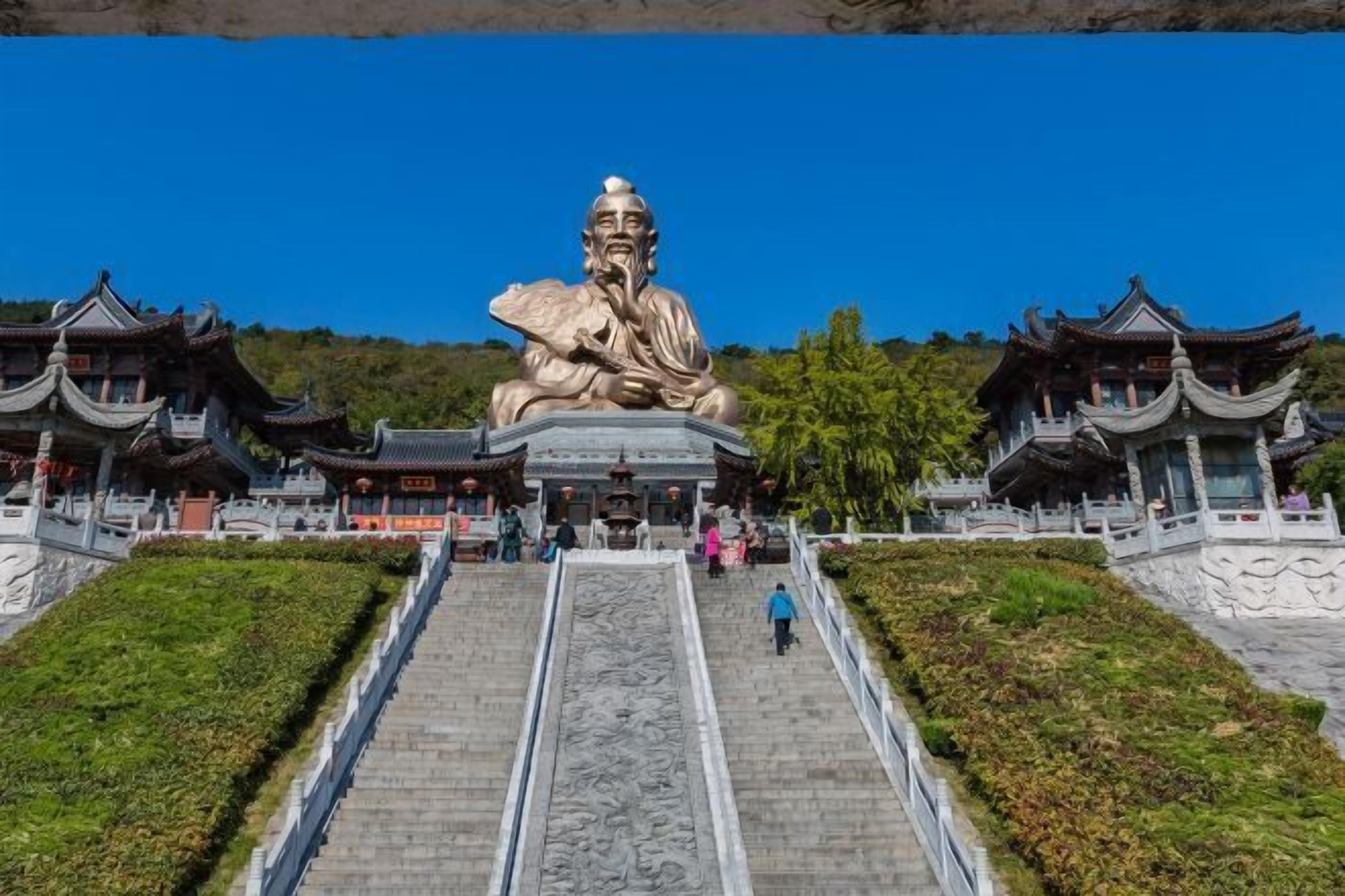A large statue of a seated figure at the top of a staircase leading to traditional buildings with ornate roofs.