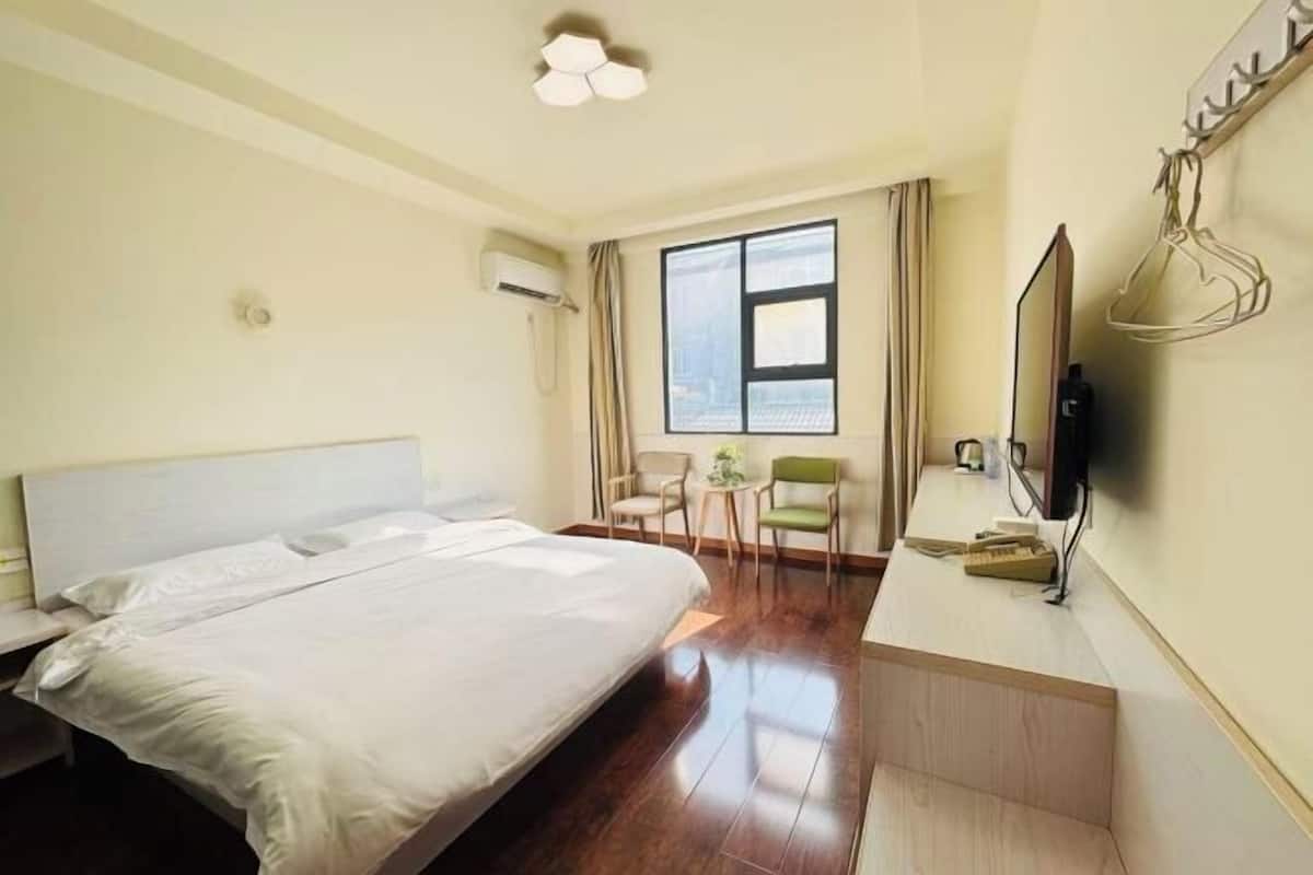 A hotel room with a bed, a desk with a computer, a TV, and a window with curtains.