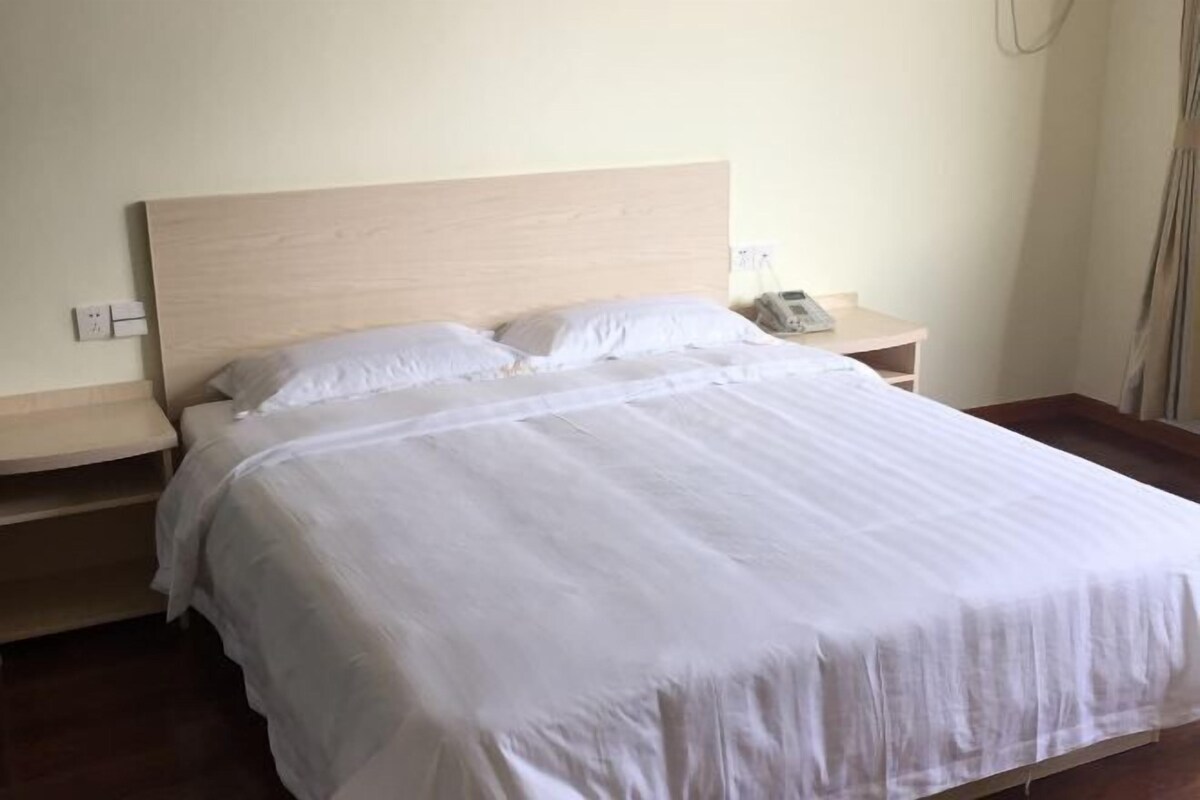 A neatly made bed with white linens, a wooden headboard, and a bedside table with a telephone.