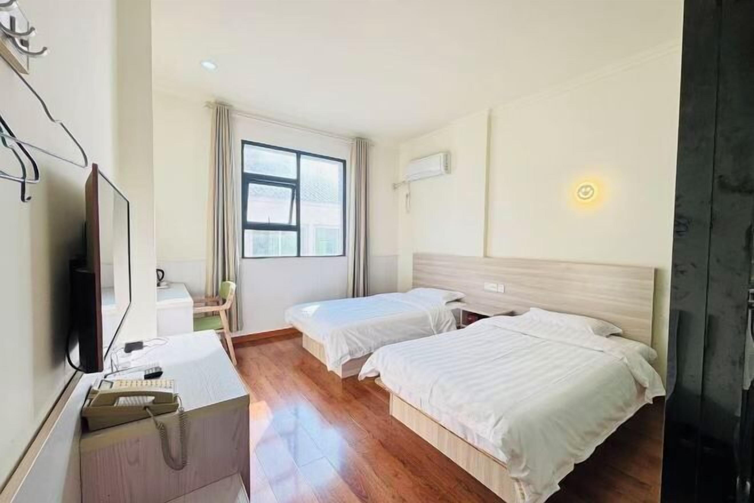 Een hotelkamer met twee bedden, een bureau met telefoon, een televisie en een raam met gordijnen.