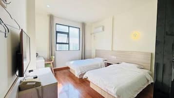 Een hotelkamer met twee bedden, een bureau met telefoon, een televisie en een raam met gordijnen.