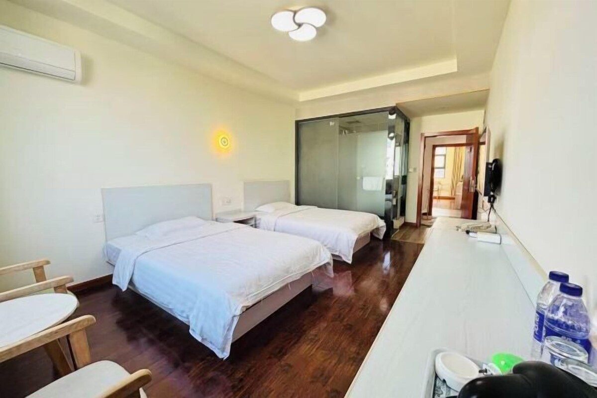 A hotel room with two beds, a desk, a chair, a mirror, and a bathroom.