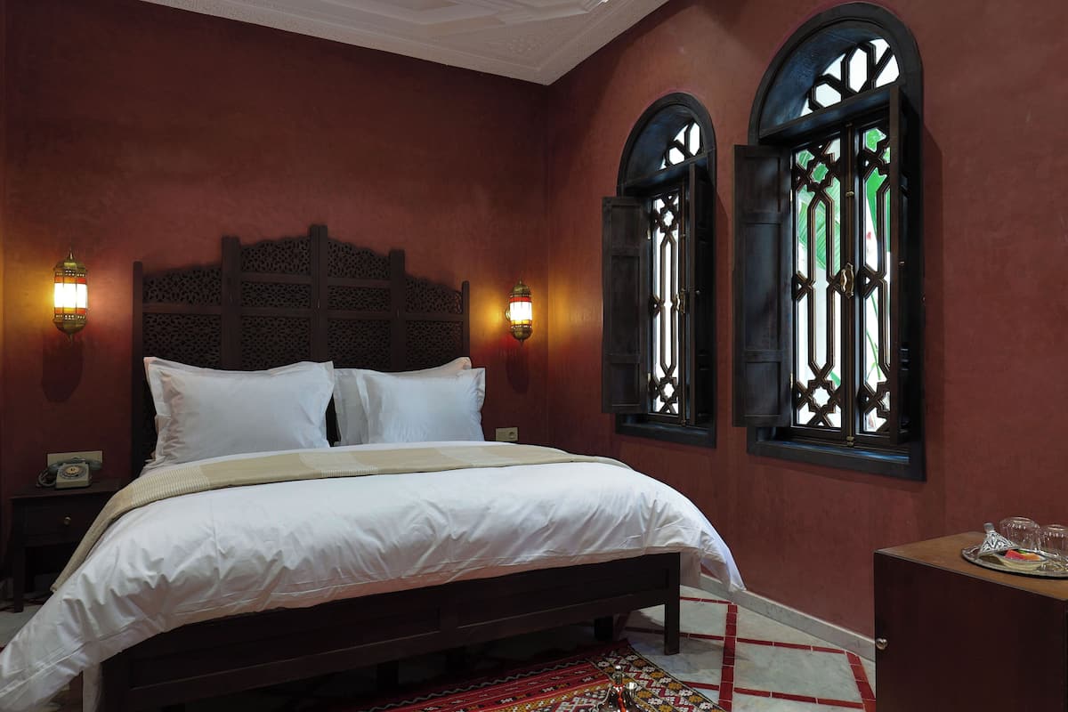 A bedroom with a large bed, two wall-mounted lamps, and a window with decorative shutters.