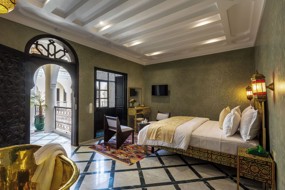 A room with a bed, a chair, a small table, a decorative lamp, and a large window.